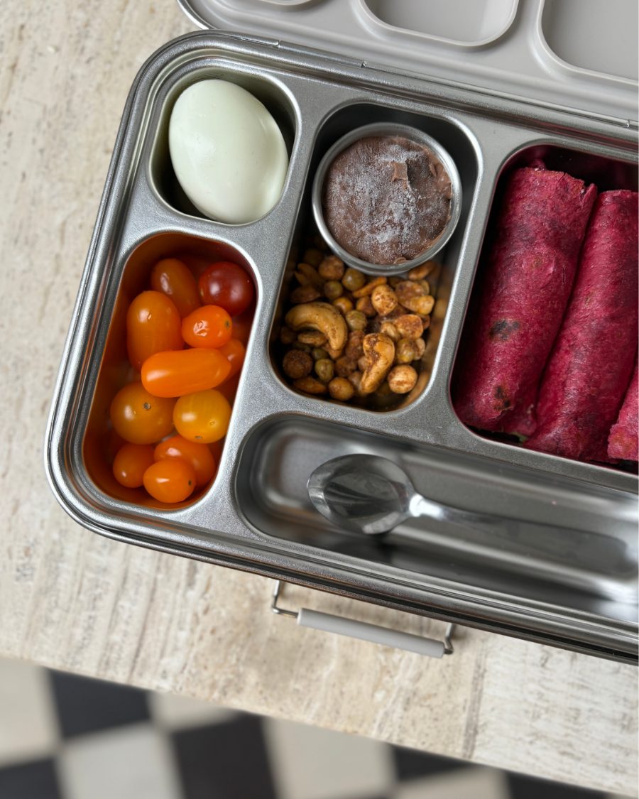 A packed lunchbox with egg, tomatoes, roasted chickpeas, chocolate dip and beet wraps