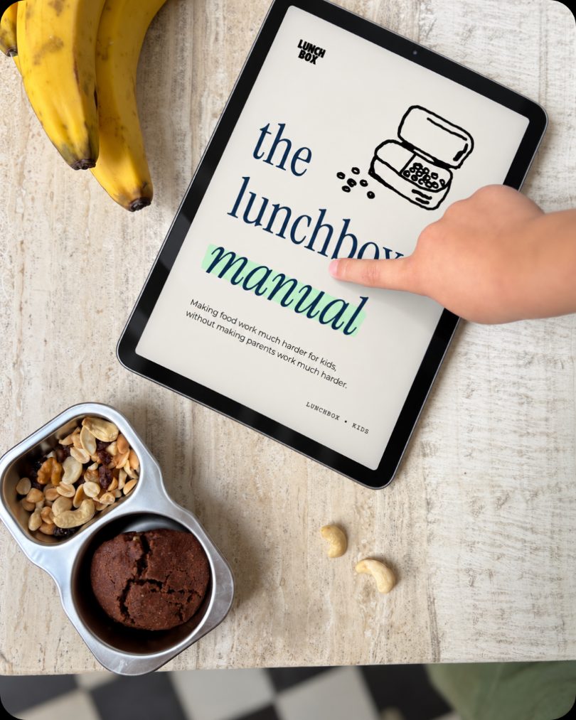 A child's finger tapping The Lunchbox Manual cover on a tablet, next to bananas and a snack tin