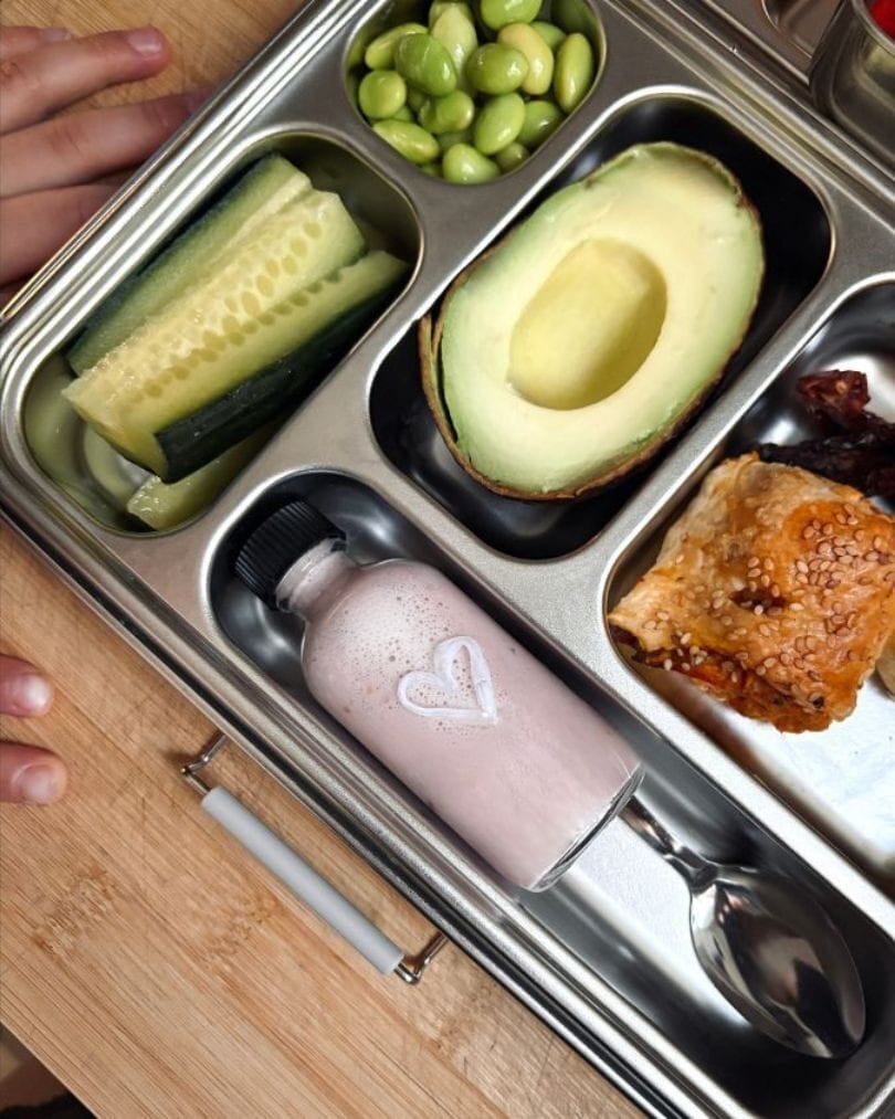 A beautifully packed lunchbox with cucumber, edamame, avocado, pastry and a pink smoothie