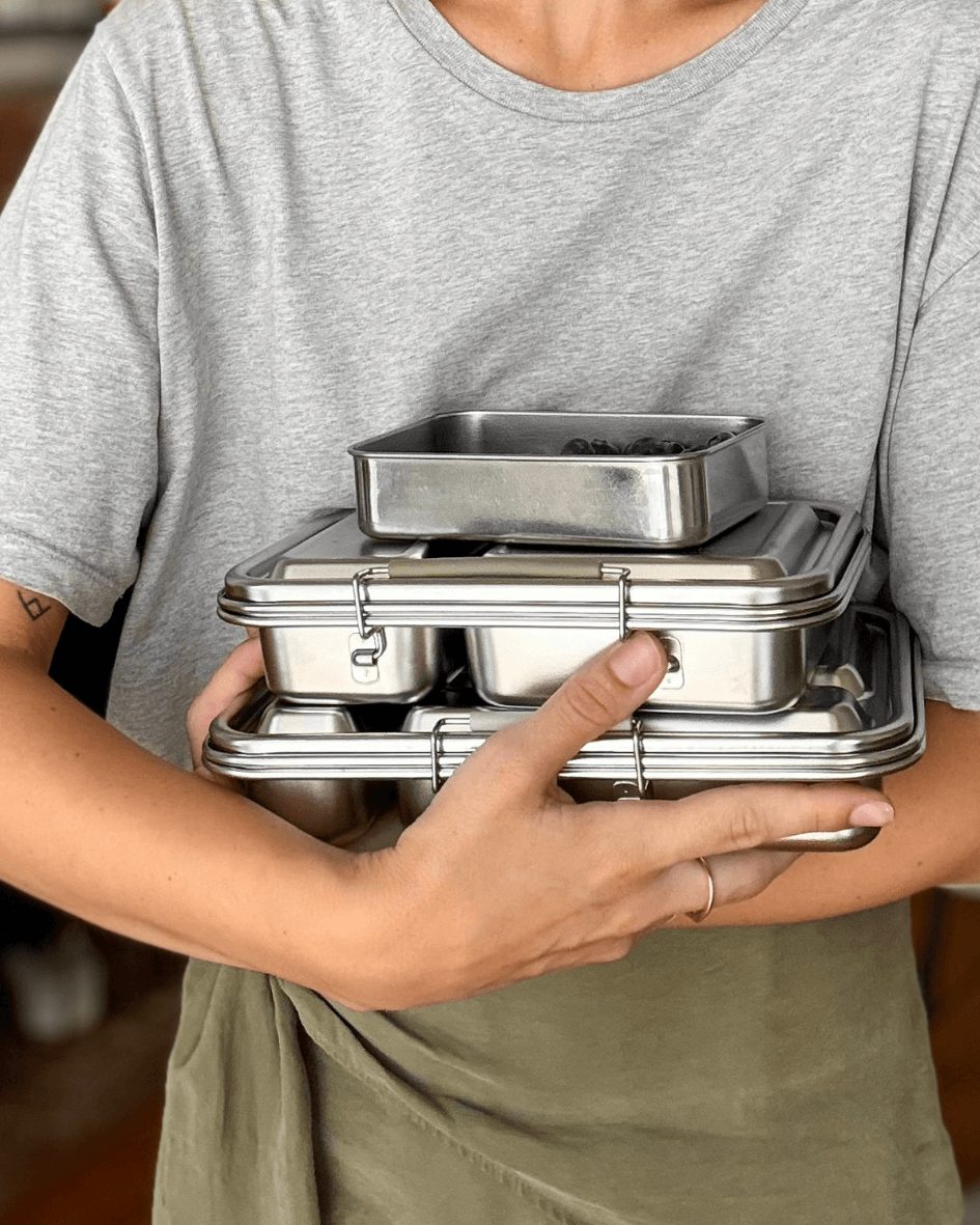 Person in a grey t-shirt holding a stack of three stainless steel bento lunchboxes